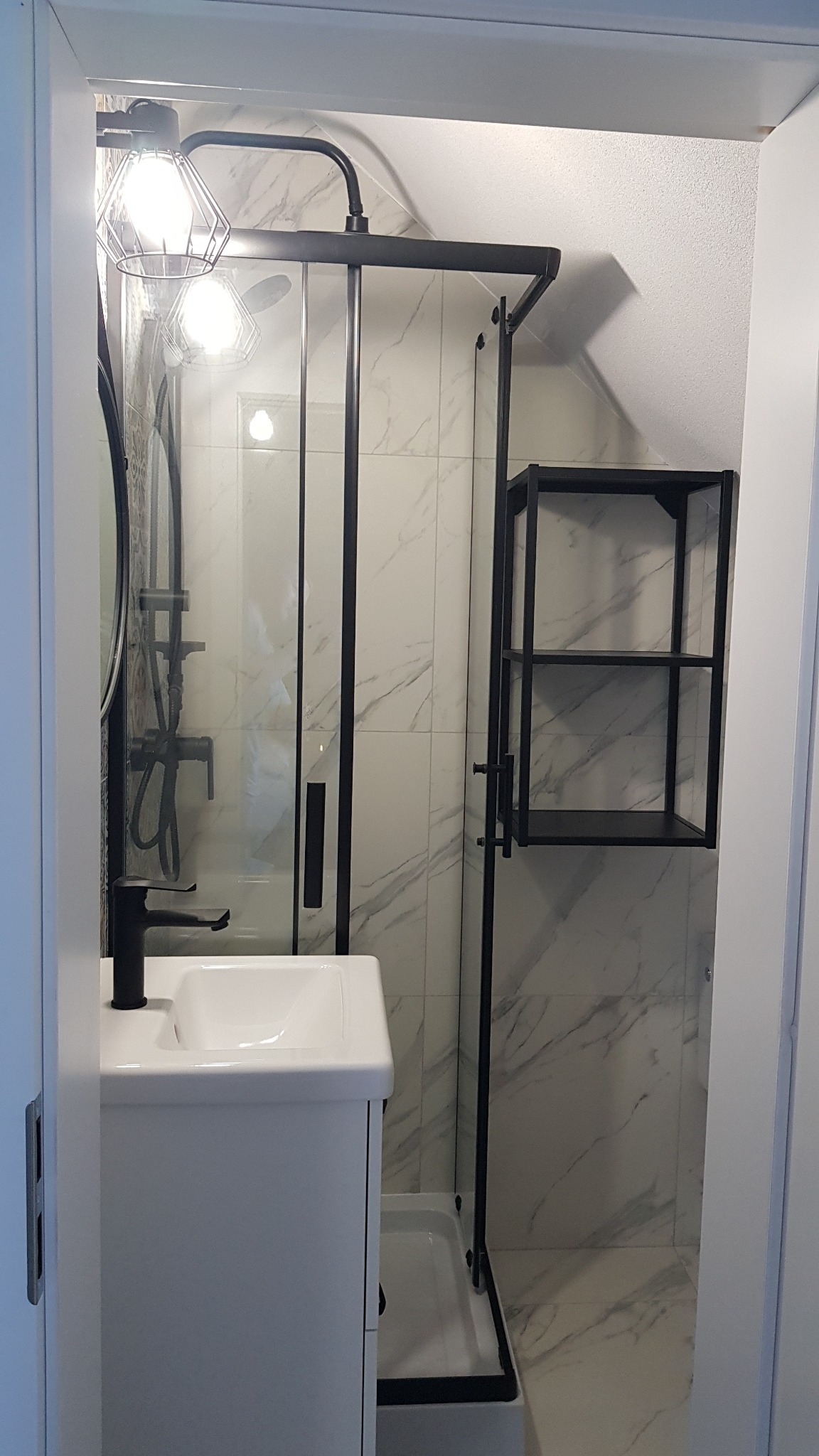 Nowoczesna łazienka w skandynawskim stylu: biała umywalka z czarną armaturą, kabina prysznicowa z czarną ramą i półka na ścianie z marmurowym wzorem.