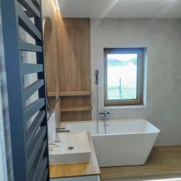 Wykonawstwo robót budowlanych - Nowoczesna łazienka z wolnostojącą wanną, umywalką nablatową i grzejnikiem drabinkowym. Drewniane akcenty i subtelne oświetlenie LED tworzą elegancki wystrój.