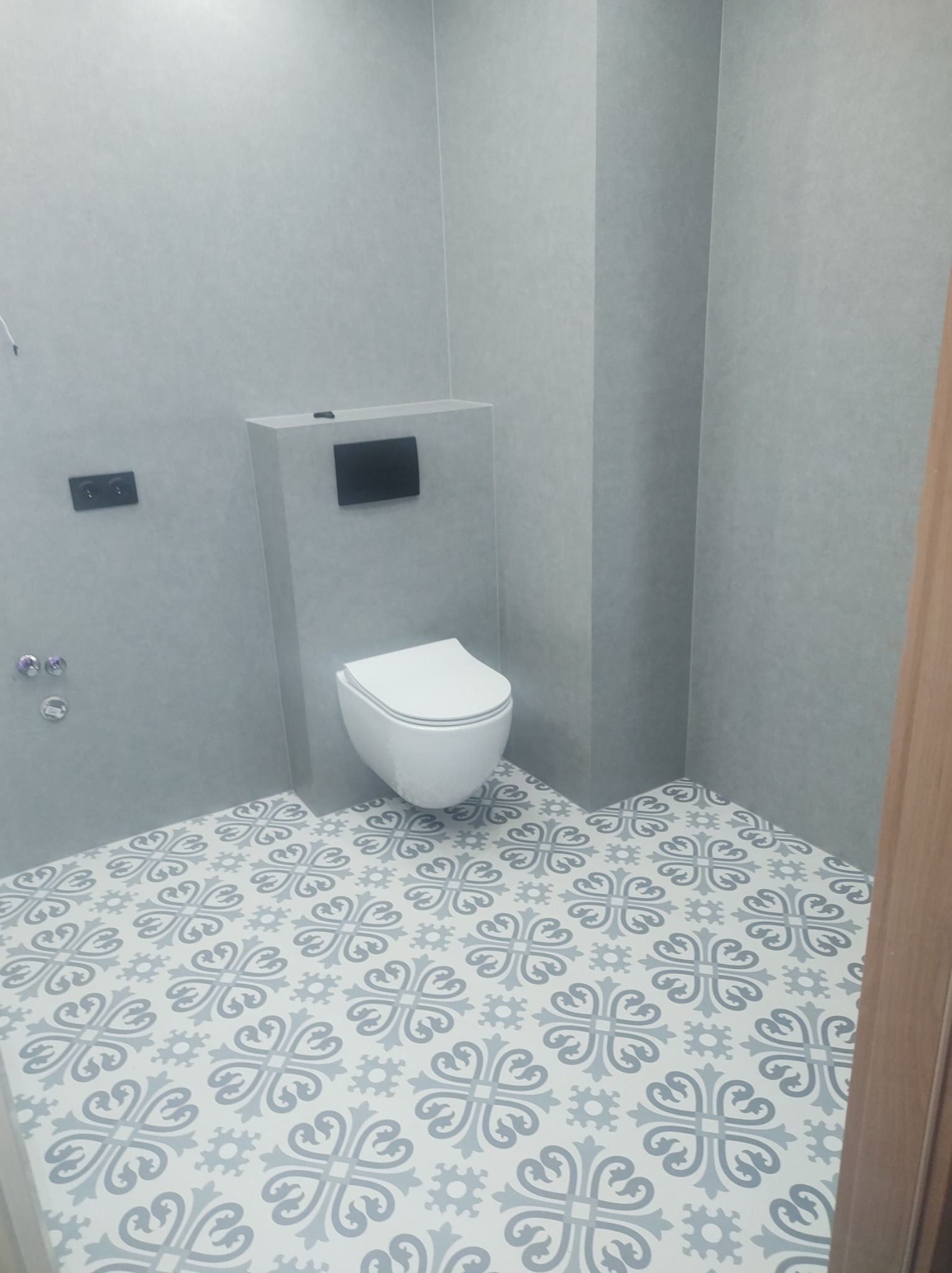 Wykończona łazienka w Ciechanowie z toaletą podwieszaną, szarymi ścianami i wzorzystą, jasną podłogą.