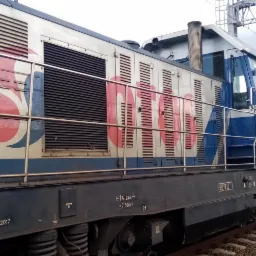 Bok lokomotywy NEWAG NS z wagonami towarowymi na torach kolejowych, widoczne detale malowania i oznaczenia techniczne.