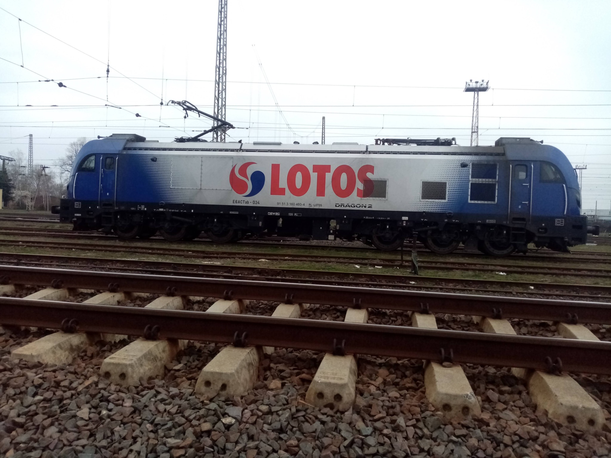 Lokomotywa Dragon 2 w barwach Lotos Kolej na torach, widok z boku, szaro-błękitna kolorystyka, betonowe podkłady kolejowe na pierwszym planie.