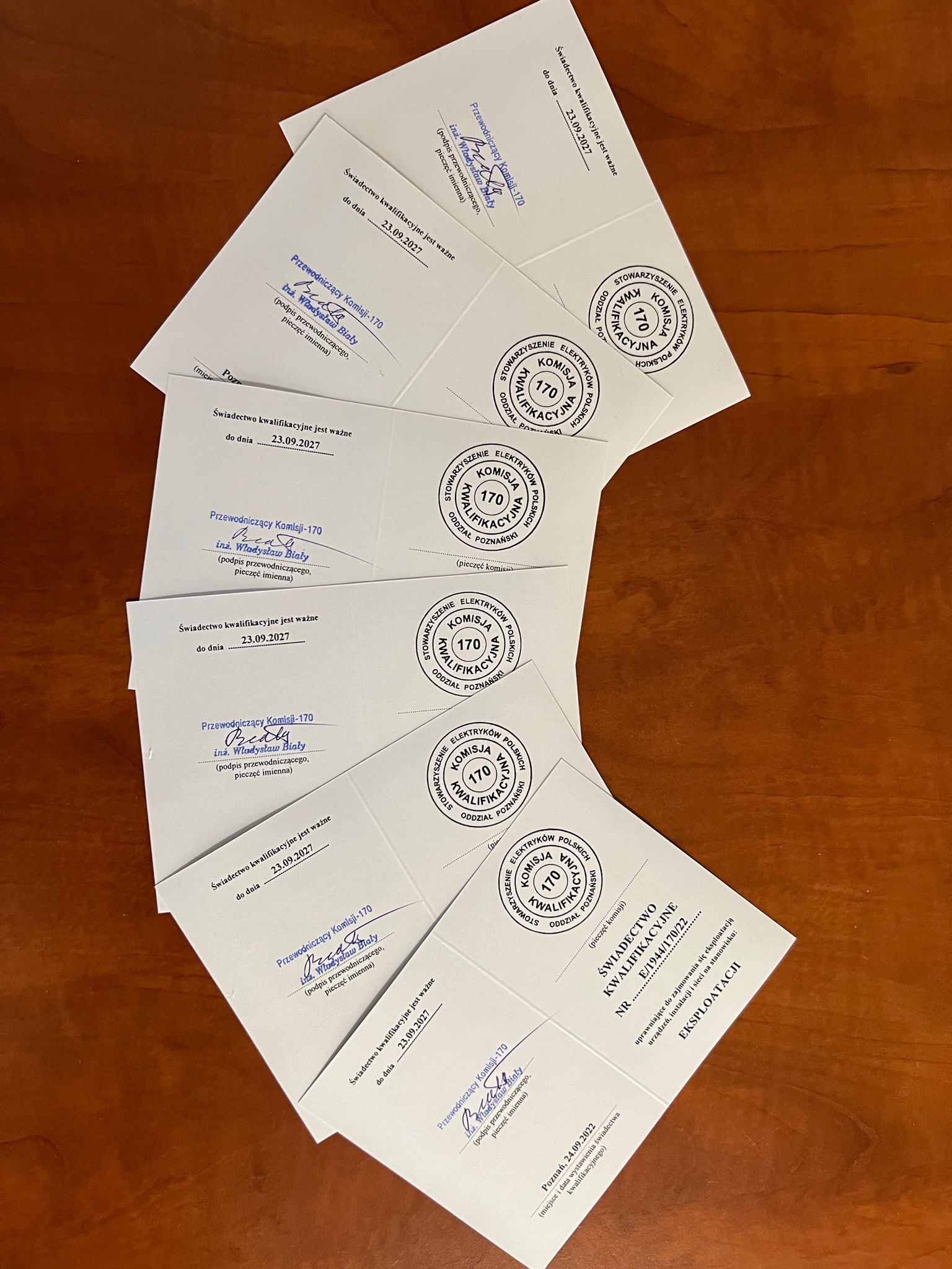 Świadectwa kwalifikacyjne elektryka z pieczęciami i podpisami przewodniczącego Komisji-170, ułożone na drewnianym biurku.
