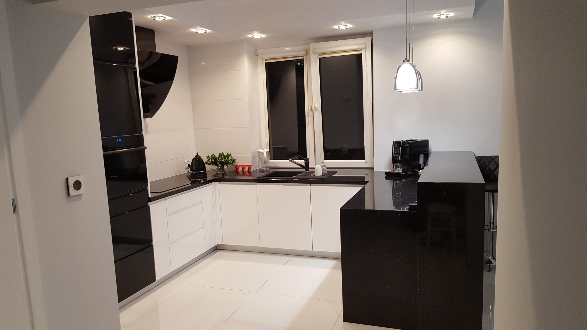 Nowoczesna kuchnia w bieli i czerni z czarnym blatem z motywem gwiazd, minimalistycznym oświetleniem i zabudową piekarnika z czarnymi frontami.