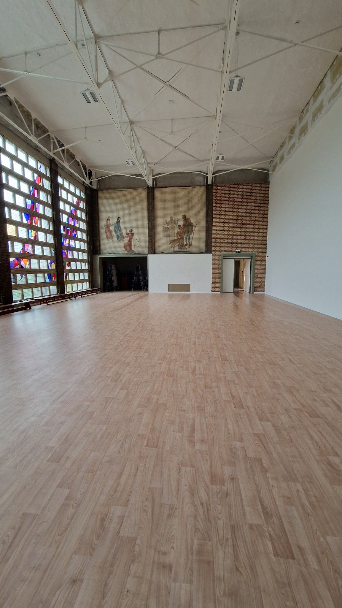 Przestronne, wysokie pomieszczenie z parkietem, mozaikami na ścianach i witrażami w oknach, po gruntownym wysprzątaniu.