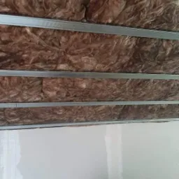 Ocieplenie poddasza wełną mineralną widoczne między metalowymi profilami sufitowymi, częściowo zakryte płytą gipsowo-kartonową w trakcie montażu.