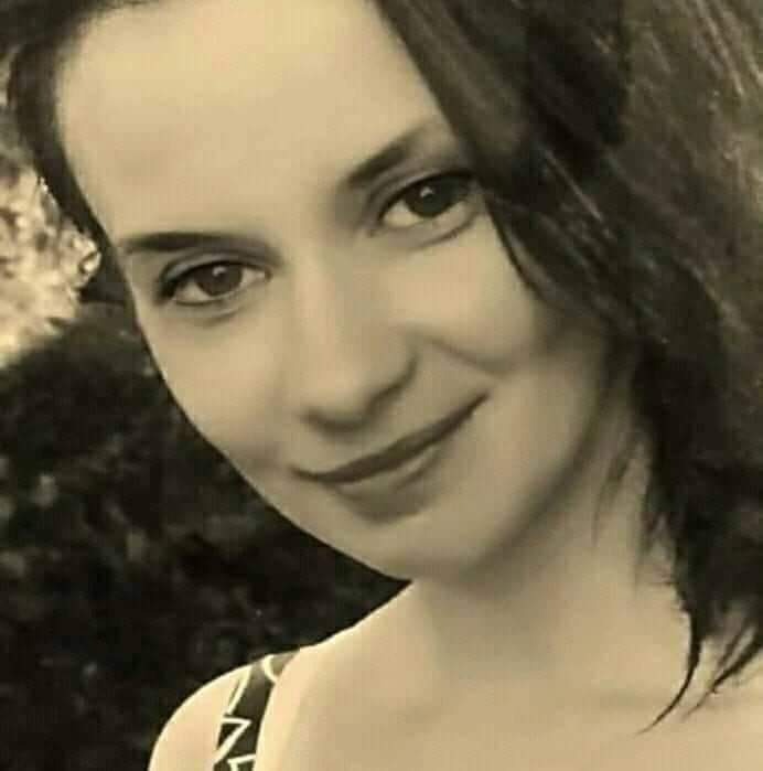 Portret uśmiechniętej kobiety z Kłodzka z ciemnymi włosami na rozmytym tle zieleni.