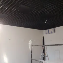 Montaż sufitu rastrowego w biurze, widoczne rusztowanie, drabina i zabezpieczony klimatyzator.