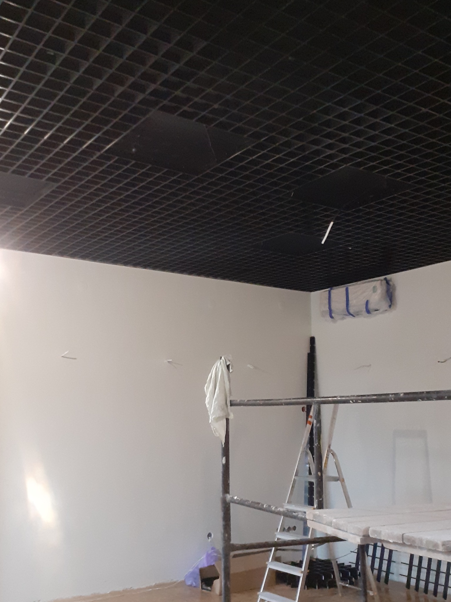 Montaż sufitu rastrowego w biurze, widoczne rusztowanie, drabina i zabezpieczony klimatyzator.