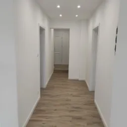 Jasny korytarz po remoncie z panelami podłogowymi imitującymi drewno i oświetleniem punktowym