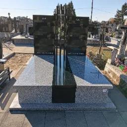 Nowoczesny nagrobek z ciemnego granitu i jasnoszarego kamienia, z metalowym krzyżem, na tle cmentarza w słoneczny dzień. Napis: 'Jezu ufam Tobie'.