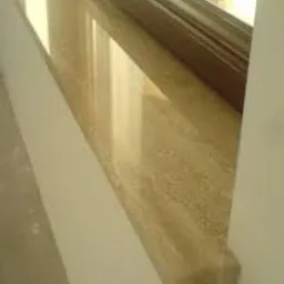 Beżowy parapet z konglomeratu z widocznym zaokrąglonym profilem krawędzi, zamontowany w białym oknie.