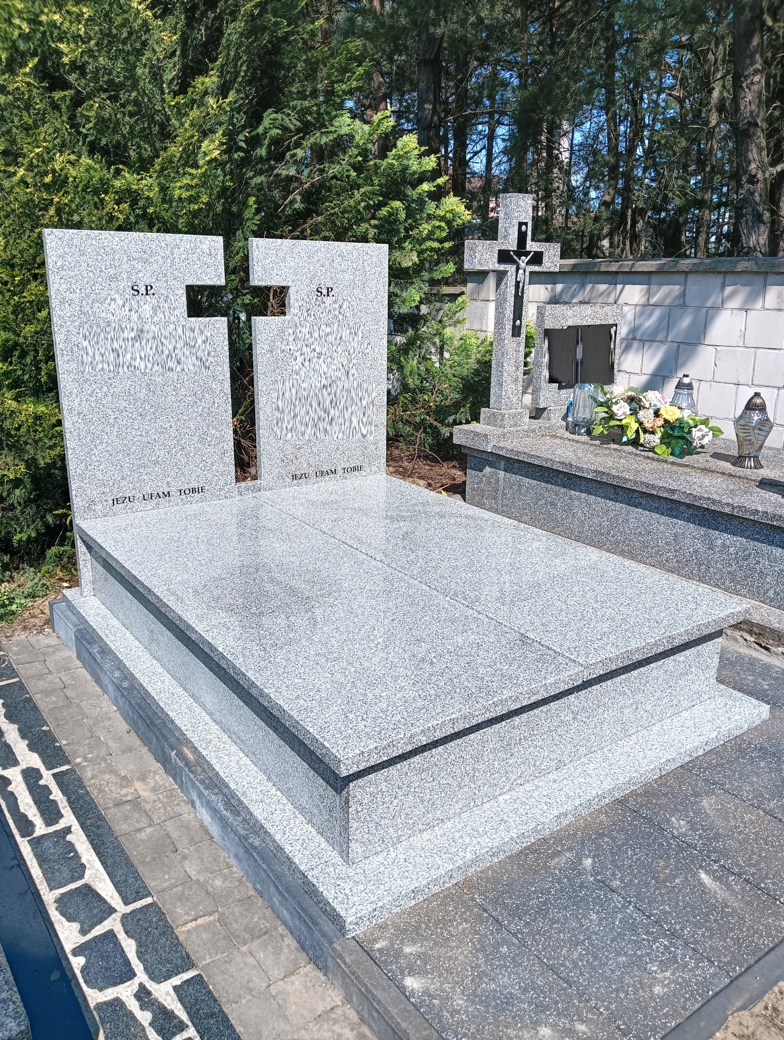 Jasnoszary, nowoczesny nagrobek z granitu z wyciętym krzyżem, inskrypcją 'Jezu Ufam Tobie' i skrótem 'S.P.' na tle zieleni cmentarnej.
