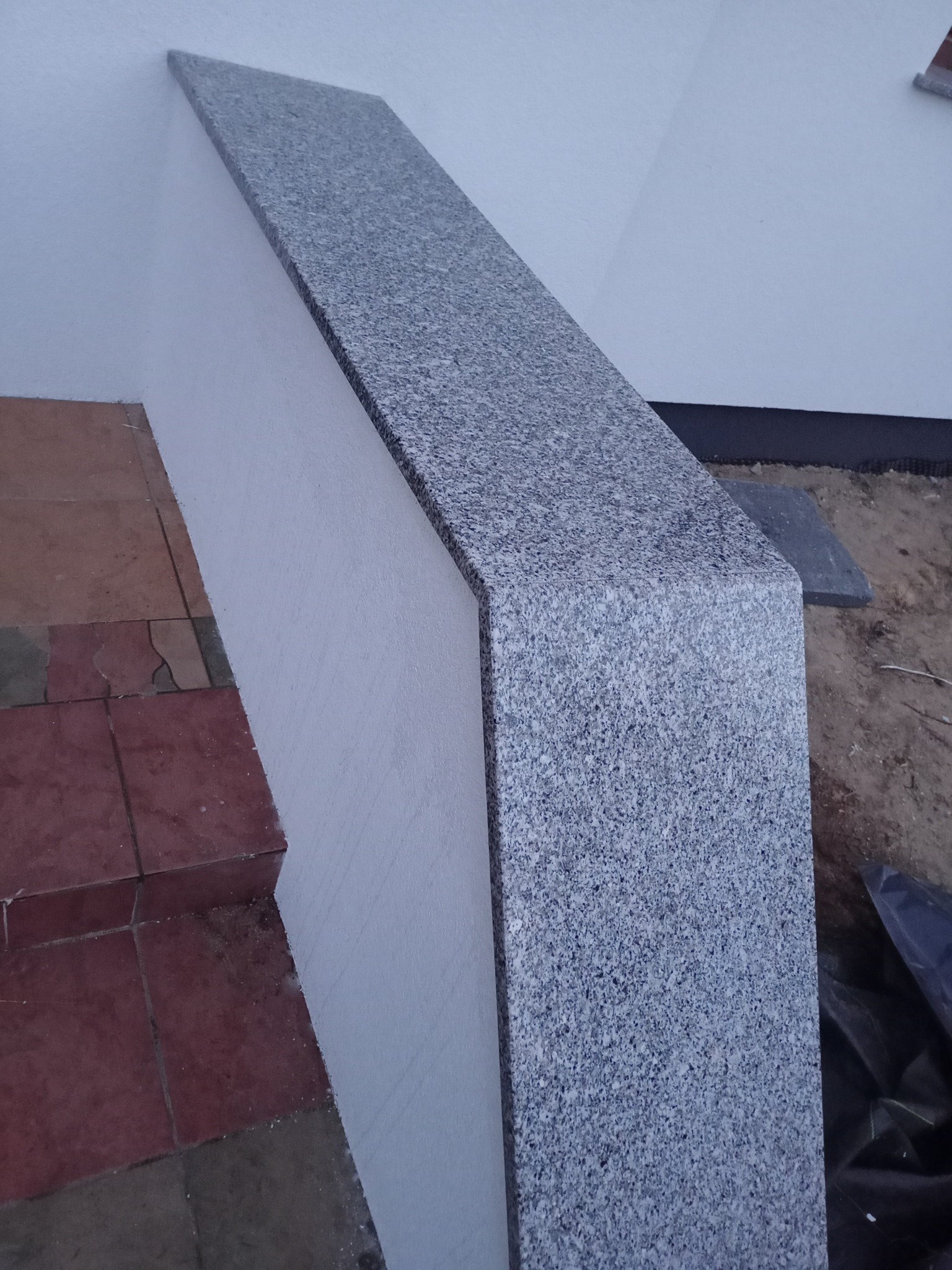 Szary parapet z konglomeratu zamontowany na murku obok schodów z płytek ceramicznych, widok z góry.