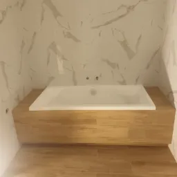 Wanna w zabudowie z drewnopodobnych paneli, ściany wyłożone płytkami imitującymi marmur, podłoga z paneli winylowych w odcieniach brązu.