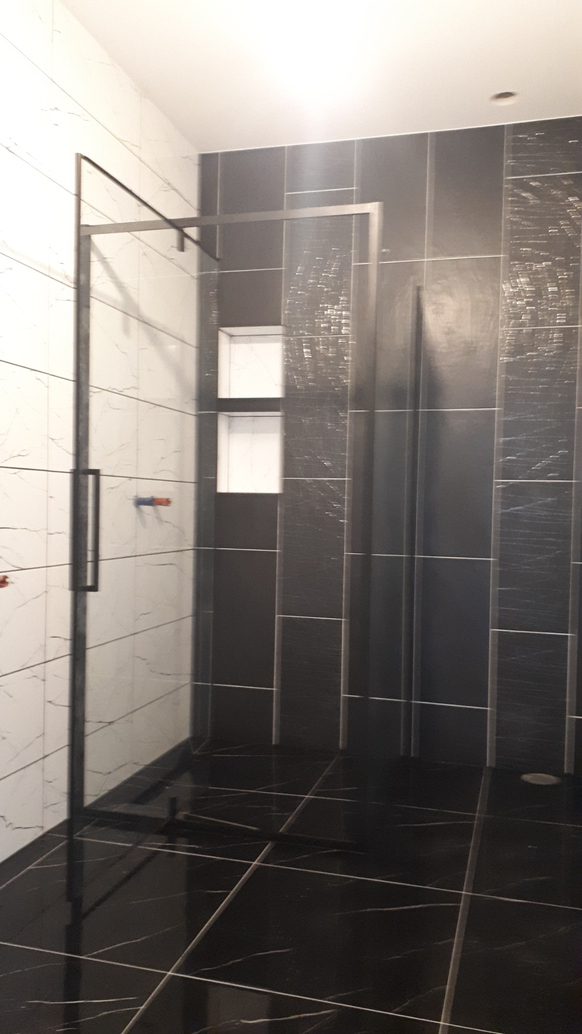 Nowoczesna łazienka z czarno-białymi płytkami, szklaną kabiną prysznicową z czarnymi profilami i wnękami w ścianie wyłożonymi białymi płytkami.