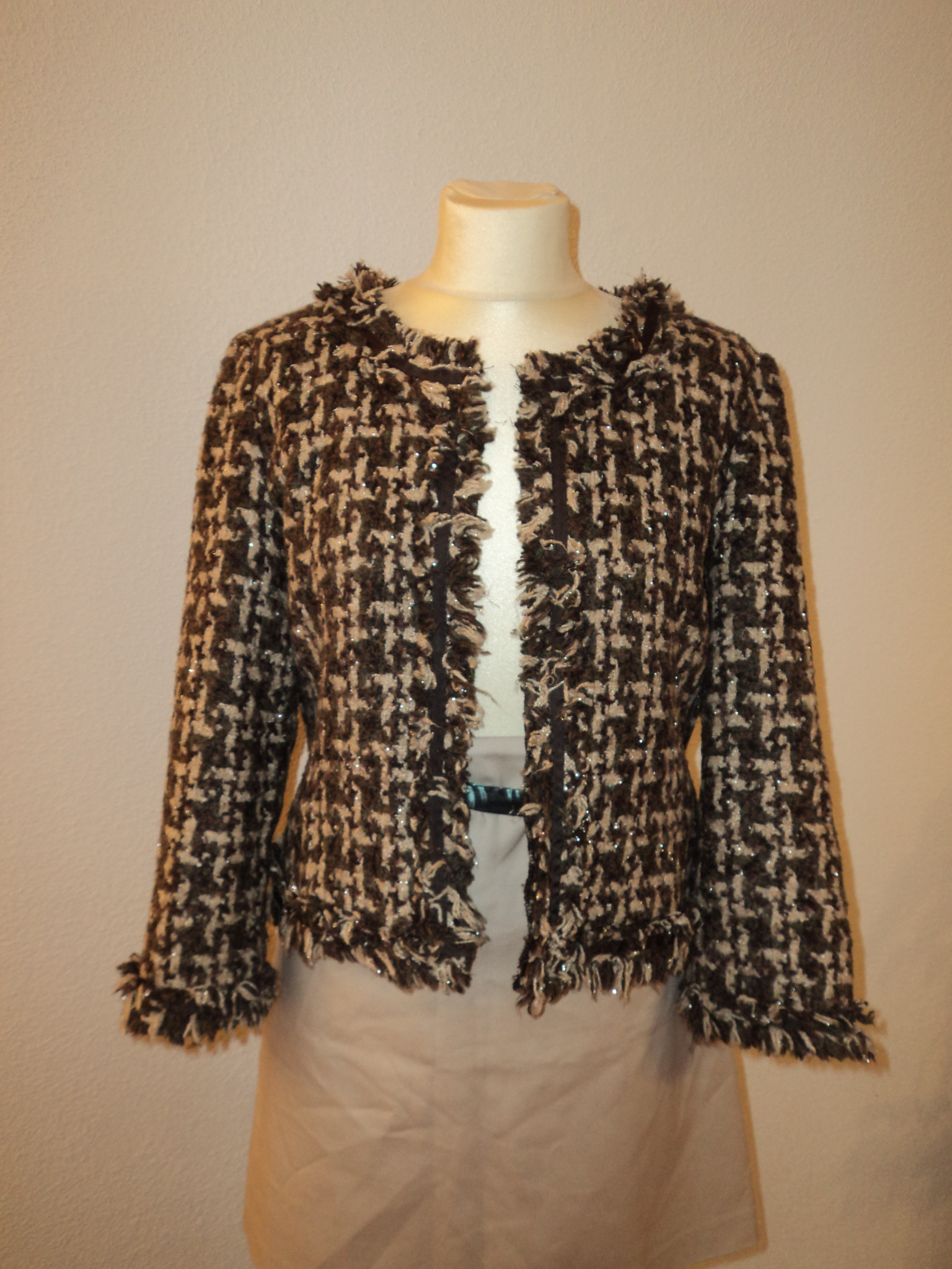 Brązowo-beżowy tweedowy żakiet z frędzlami i błyszczącymi detalami, prezentowany na manekinie z beżową spódnicą.