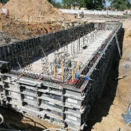 Szczegółowy widok na szalunek i zbrojenie fundamentu żelbetowego w wykopie, widoczne elementy konstrukcyjne i przygotowanie do betonowania.