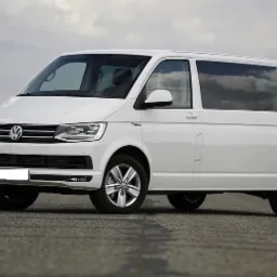 Biały Volkswagen Transporter T6 z długim rozstawem osi na asfaltowej drodze, widok z boku.