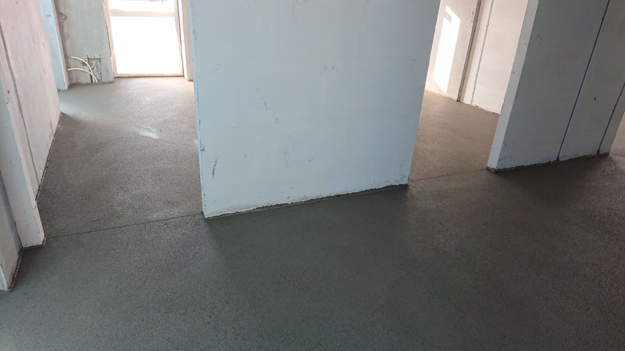 Świeżo wylana, gładka posadzka jastrychowa w surowym wnętrzu budynku, widoczne białe ściany i otwory drzwiowe.