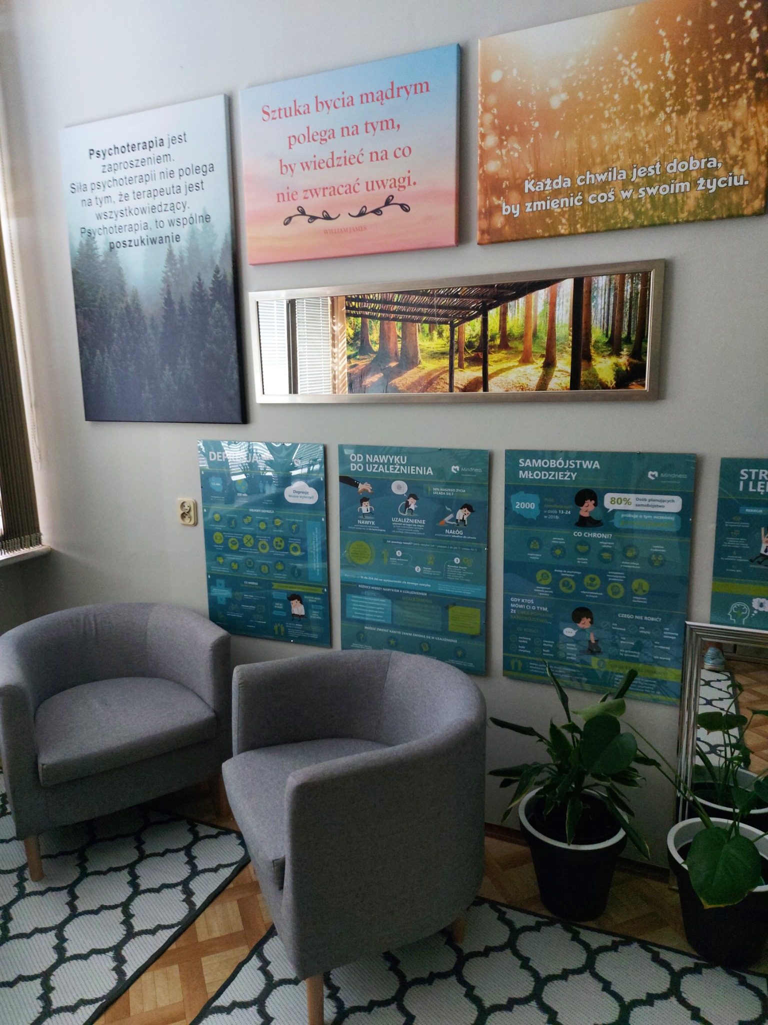 Gabinet terapeutyczny: dwa szare fotele, dywan w geometryczny wzór, plakaty edukacyjne o depresji, uzależnieniach i samobójstwach młodzieży, lustro z leśnym motywem i obrazy z cytatami na ścianie.