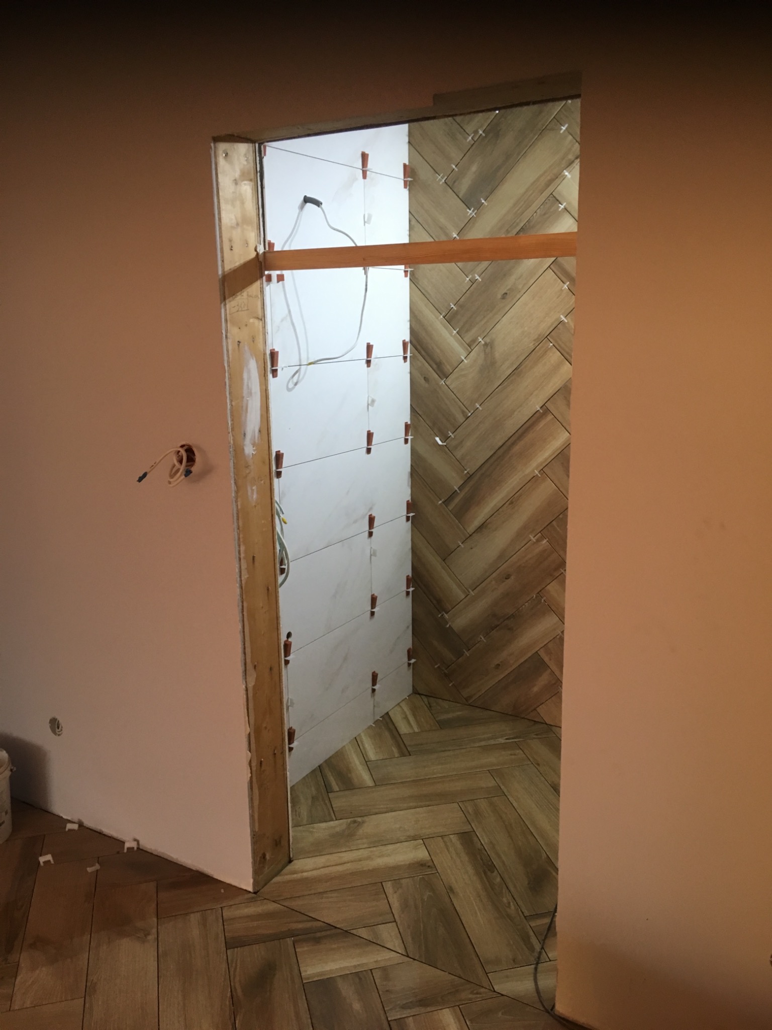 Układanie płytek w jodełkę na podłodze i ścianie w Zamościu, widoczne białe płytki w trakcie montażu na ścianie z krzyżykami dystansowymi.