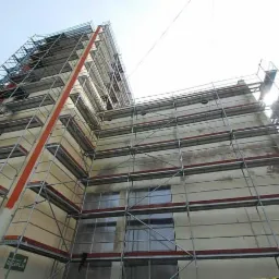 Budynek w Pabianicach w trakcie renowacji elewacji, otoczony rusztowaniami, widok z dołu.