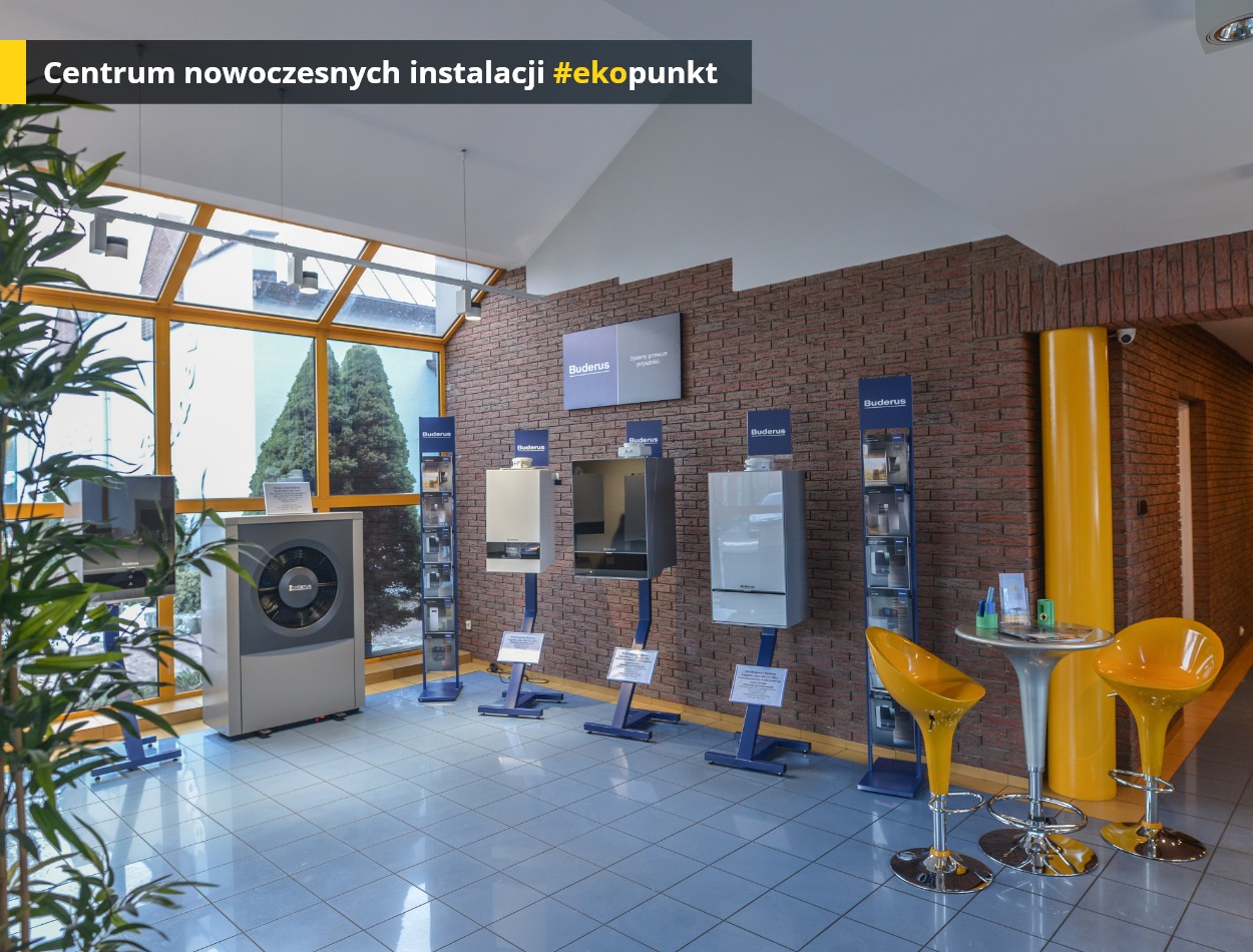 Ekspozycja pomp ciepła i kotłów grzewczych Buderus w salonie z ceglaną ścianą, widok na zewnątrz przez okno, żółte krzesła barowe przy stoliku.