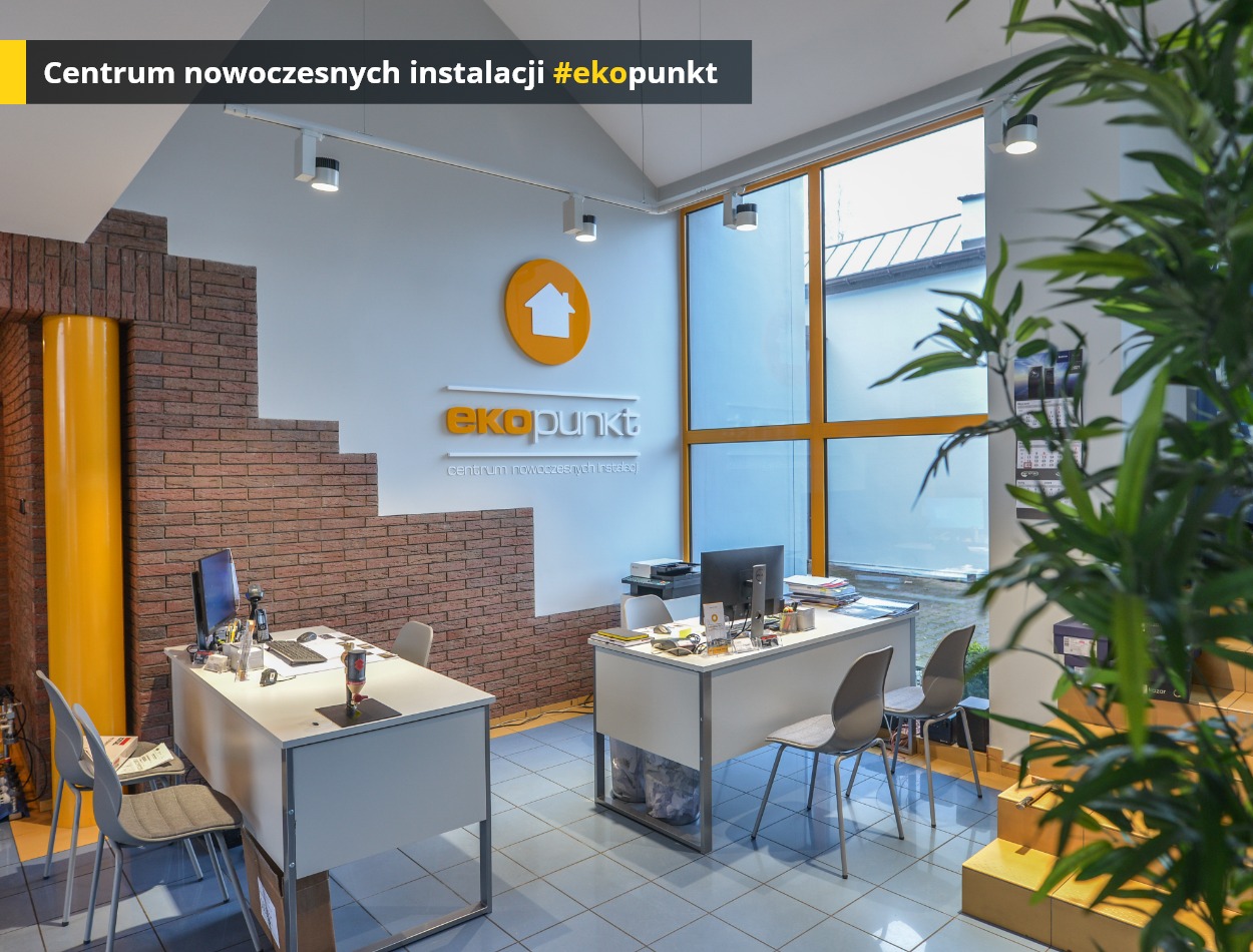 Jasne biuro firmy instalacyjnej z logo 'ekopunkt' na ścianie, biurkami, komputerami i dekoracyjną ścianą z cegły oraz dużym oknem