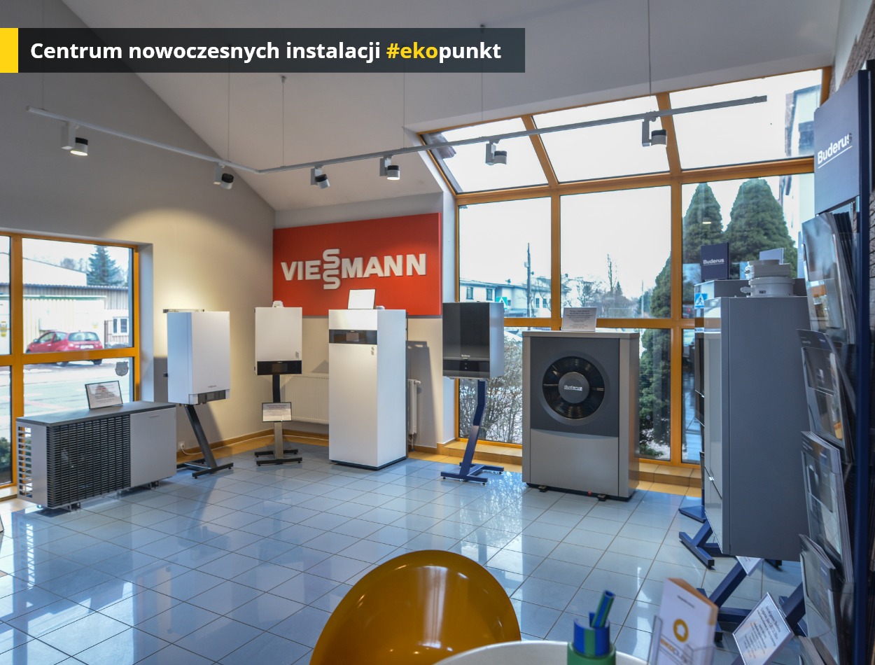 Ekspozycja nowoczesnych urządzeń grzewczych marek Viessmann i Buderus w salonie, widoczne pompy ciepła i kotły grzewcze na tle okna z widokiem na zewnątrz.