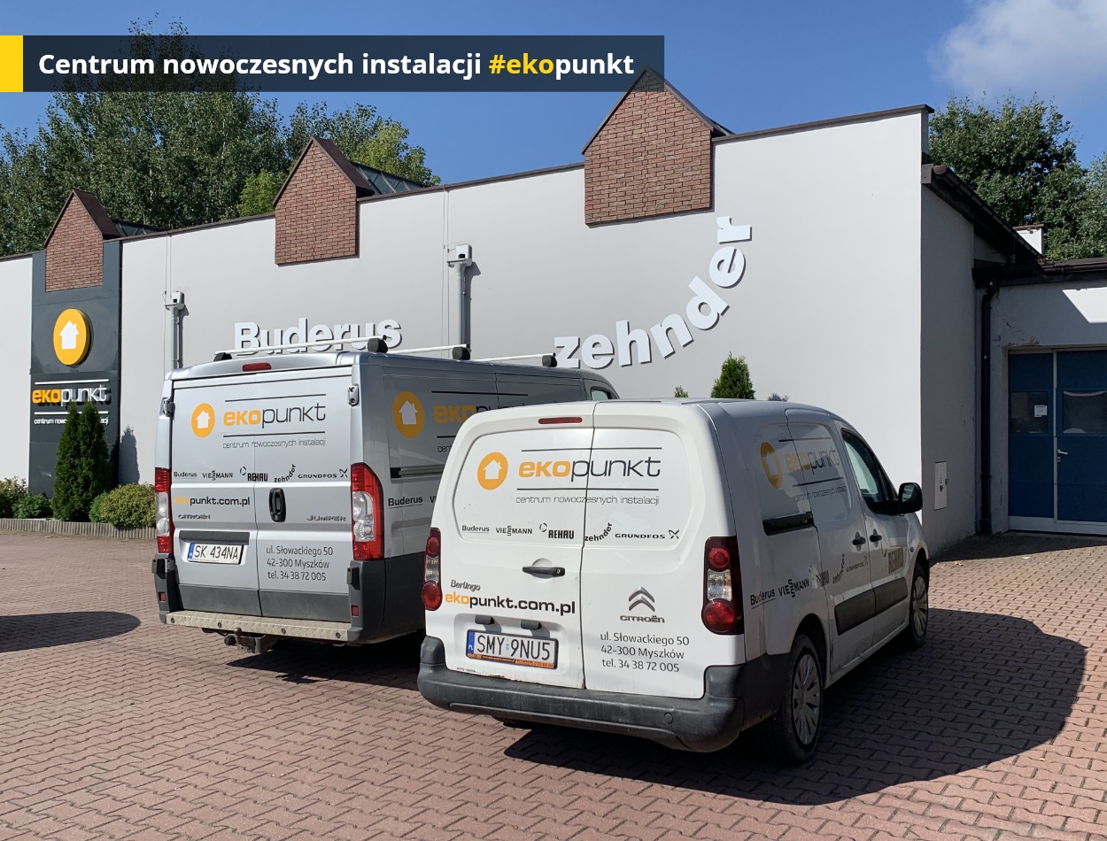 Dwa samochody dostawcze z logo firmy instalacyjnej 'ekopunkt' zaparkowane przed budynkiem z nazwami producentów: Buderus i Zehnder.
