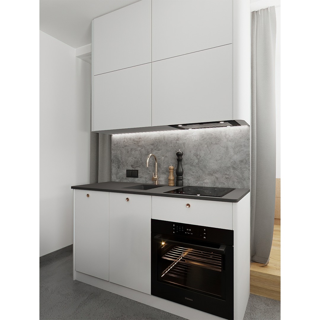 Kompaktowa kuchnia w minimalistycznym stylu: białe szafki z okrągłymi uchwytami, szary blat, złota bateria, płyta indukcyjna i piekarnik Bosch. Ściana nad blatem wykończona szarym tynkiem...