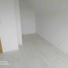 Puste poddasze w trakcie remontu, widoczne kable elektryczne wystające ze ściany, białe ściany i jasna podłoga.