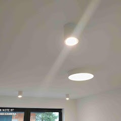 Biały sufit z czterema nowoczesnymi, okrągłymi lampami LED wpuszczanymi i natynkowymi, emitującymi jasne światło w minimalistycznym wnętrzu.