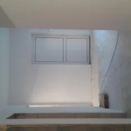 Wnętrze w trakcie remontu, widoczne schody, okno PCV i fragment ściany z nierówną powierzchnią.