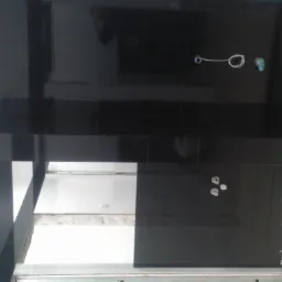 Częściowo wykończona łazienka z czarnymi, błyszczącymi płytkami, widoczne otwory na armaturę i fragmenty niezabezpieczonej ściany.