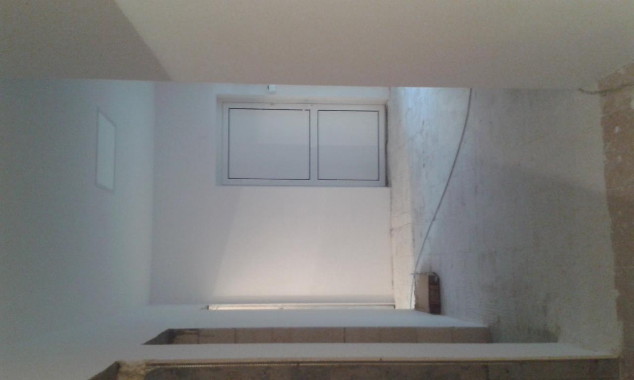 Wnętrze w trakcie remontu, widoczne schody, okno PCV i fragment ściany z nierówną powierzchnią.