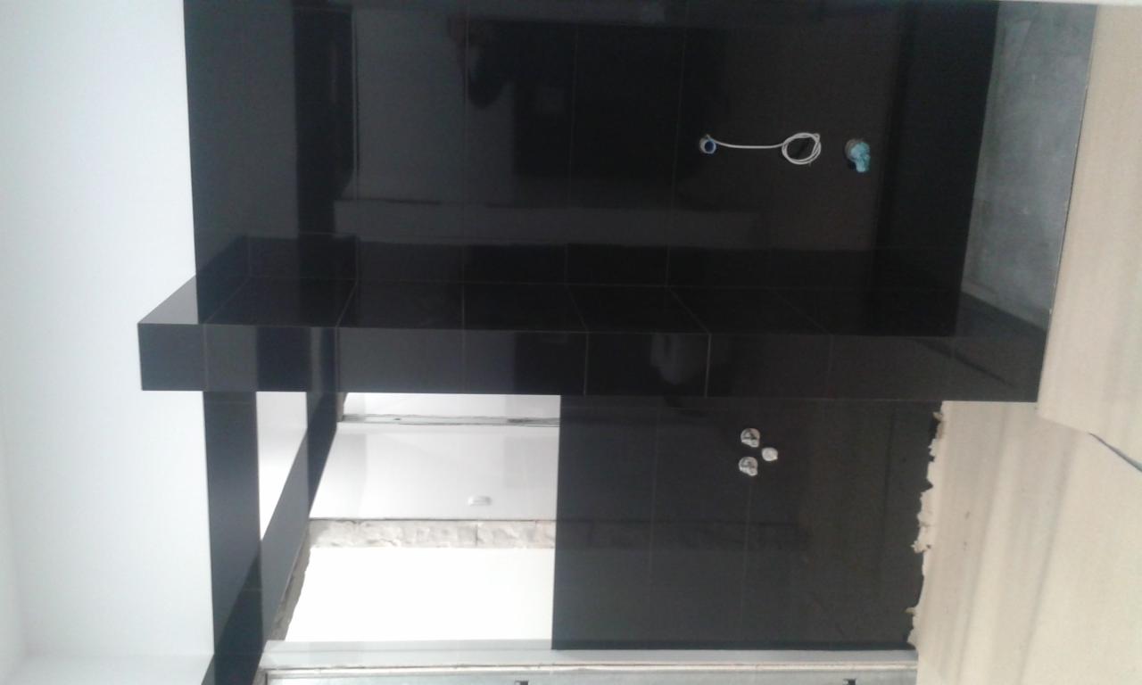 Częściowo wykończona łazienka z czarnymi, błyszczącymi płytkami, widoczne otwory na armaturę i fragmenty niezabezpieczonej ściany.