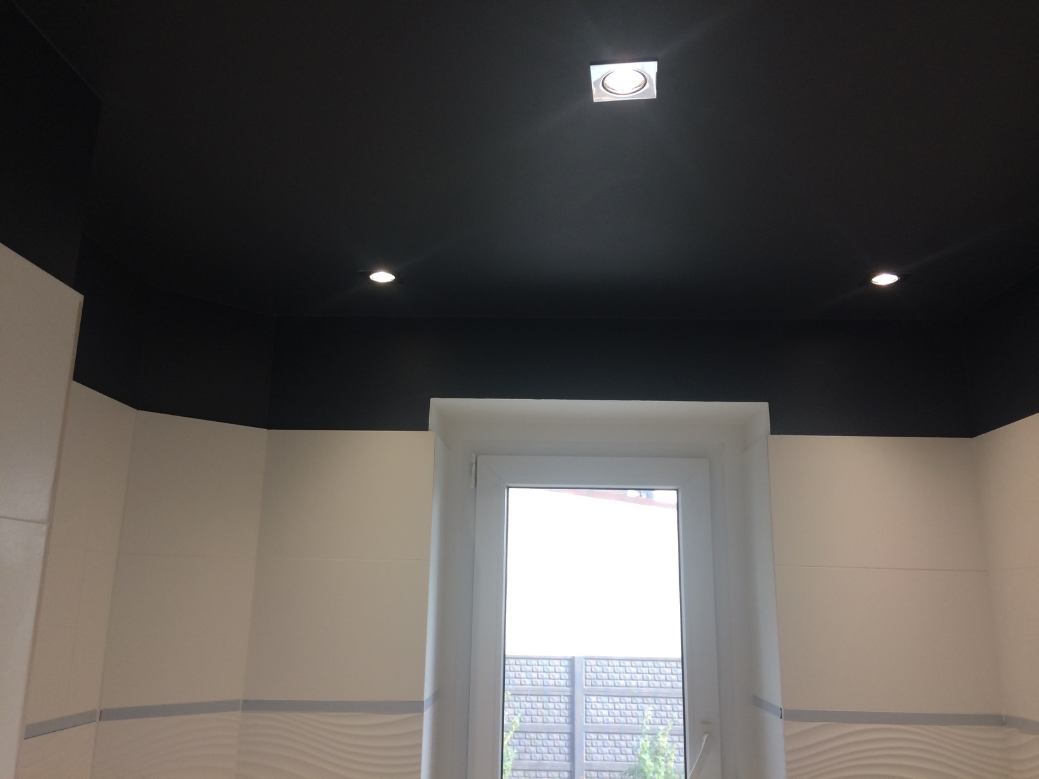 Czarne podwieszane sufity z trzema punktowymi źródłami światła w nowocześnie wykończonym wnętrzu, widok na białe ściany i okno.