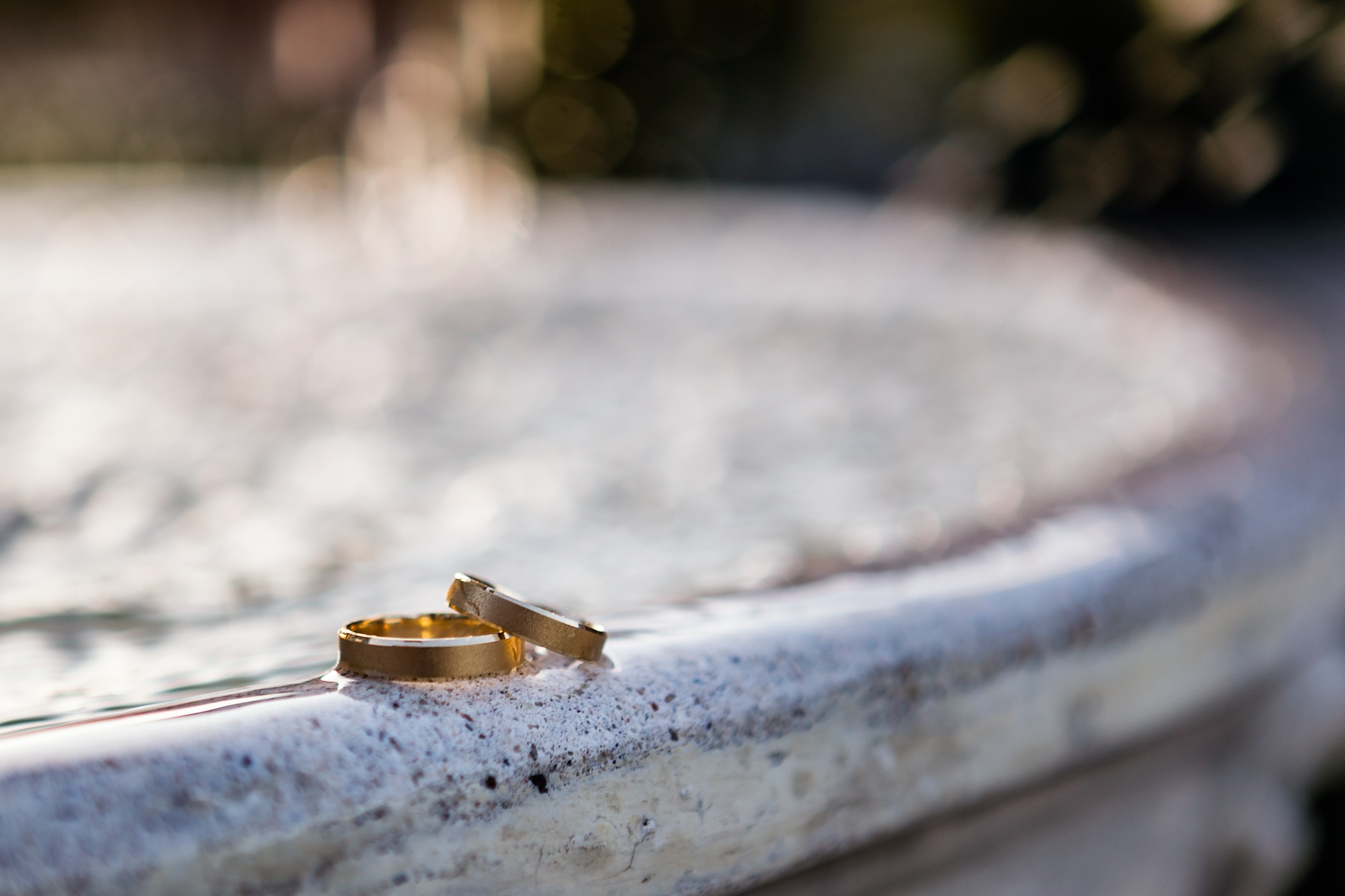 Dwa złote obrączki ślubne leżące obok siebie na jasnym, marmurowym blacie z rozmytym tłem.