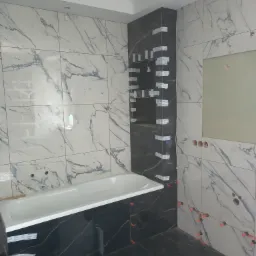 Łazienka w trakcie wykańczania: białe i czarne płytki imitujące marmur na ścianach i podłodze, widoczna wanna, poziomice i krzyżyki dystansowe do płytek.