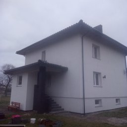 TOM-BUD Tomasz Mielczarek - Dwukondygnacyjny dom z jasną elewacją po renowacji, widoczne pozostałości materiałów budowlanych i drewniana ławka przed wejściem.