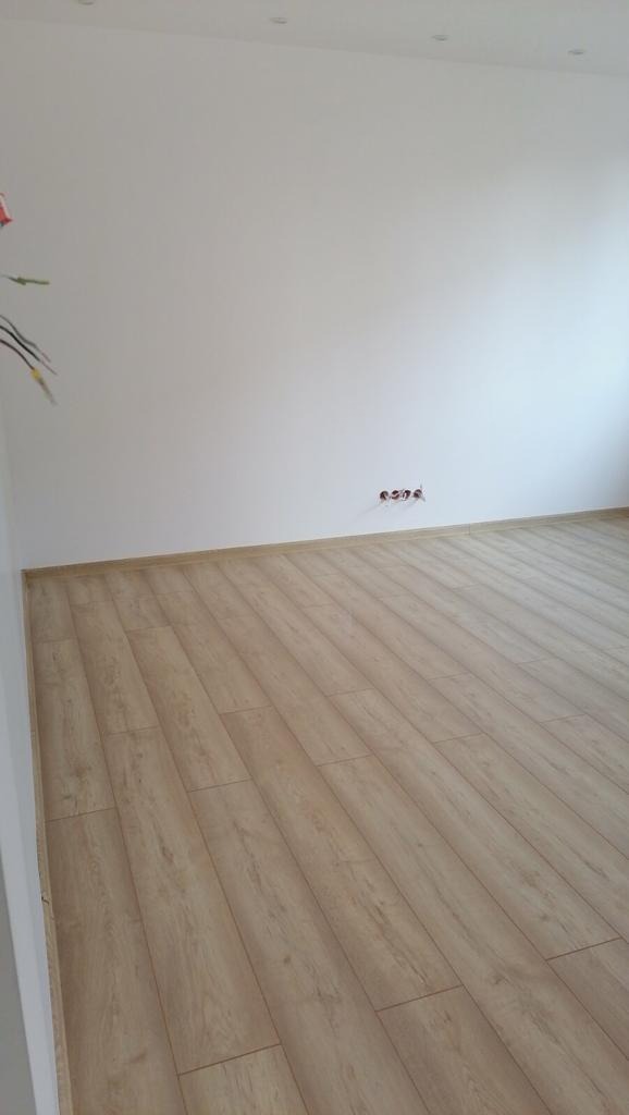 Jasne panele podłogowe ułożone w nowym pokoju z białymi ścianami i wystającymi przewodami elektrycznymi