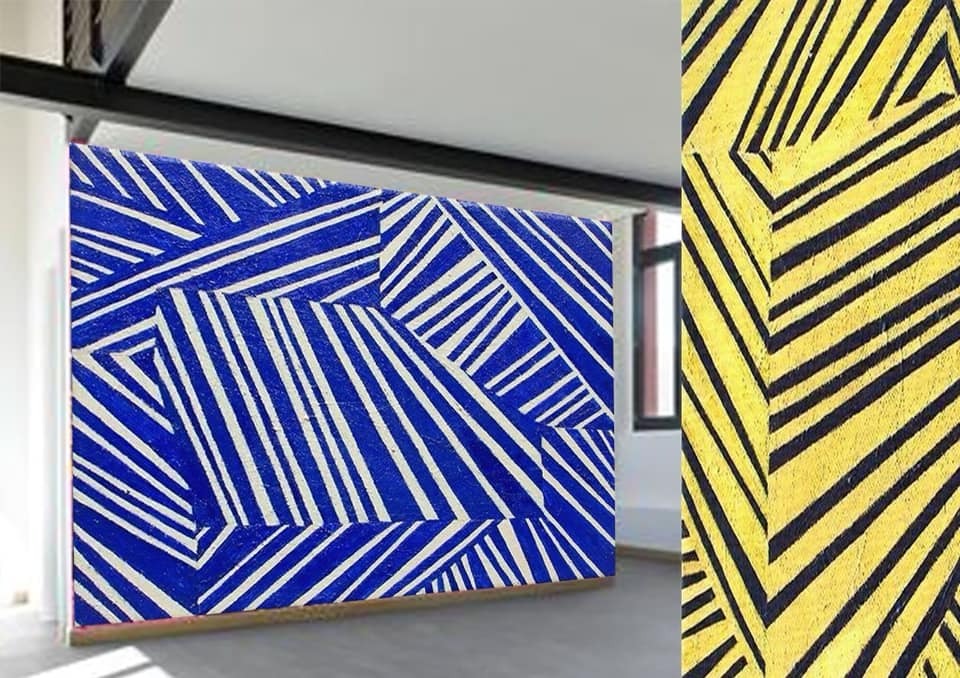 Abstrakcyjna kompozycja ścienna z niebiesko-białymi ukośnymi pasami po lewej i żółto-czarnymi ukośnymi pasami po prawej stronie, tworząca geometryczny wzór na ścianie w jasnym wnętrzu.
