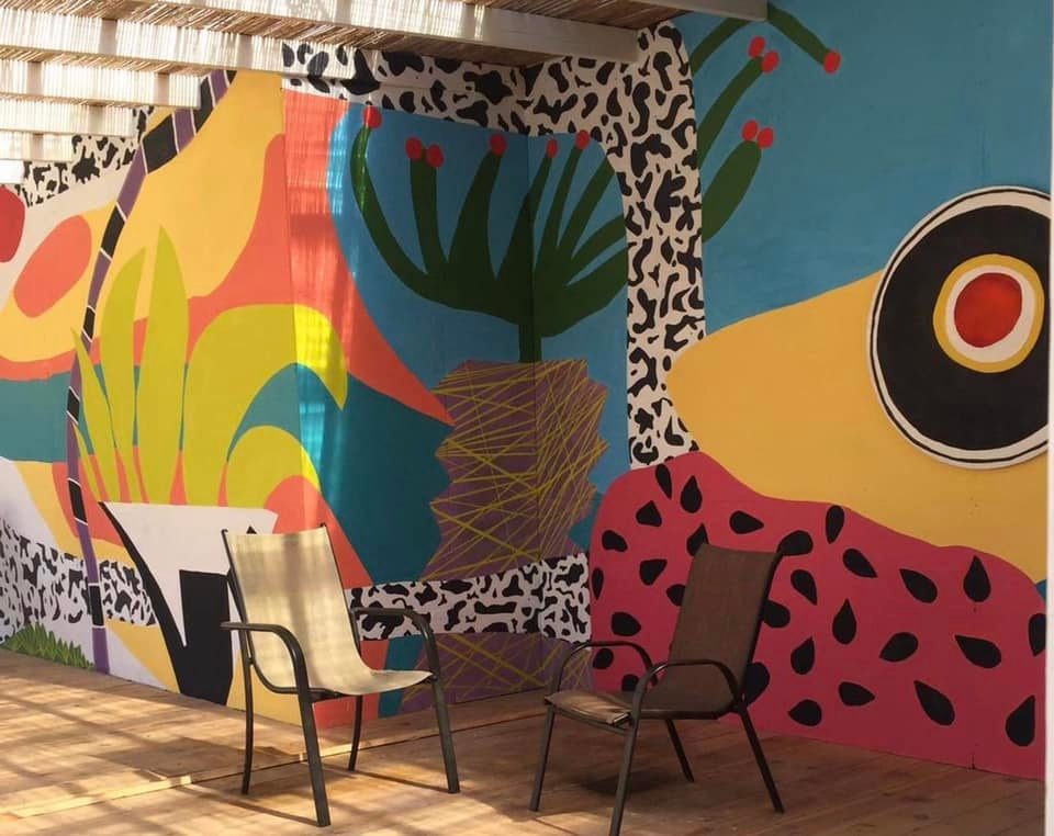 Kolorowa, abstrakcyjna malowanka na ścianie z dwoma krzesłami na drewnianej podłodze pod zadaszeniem.