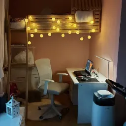 Pokój w Płocku z antresolą do spania, oświetlony girlandą z kulistych lampek, biurkiem z laptopem i krzesłem biurowym, na podłodze panele.