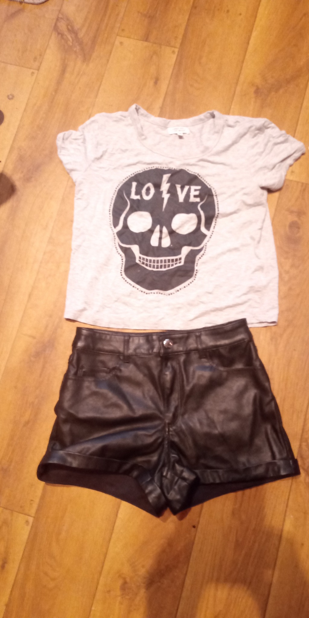 T-shirt z nadrukiem czaszki z napisem LOVE i czarne, skórzane szorty leżące na drewnianej podłodze.