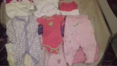 Różnorodny zestaw ubranek niemowlęcych w odcieniach bieli, różu i szarości z delikatnymi wzorami leżących na beżowym tle.