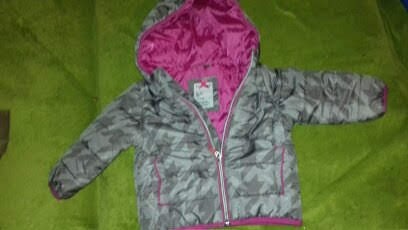 Dziecięca kurtka puchowa w odcieniach szarości z motywem gwiazd, z różową podszewką i kapturem, rozłożona na zielonym tle.