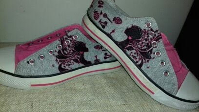 Para szarych tenisówek z różowymi wstawkami i czarnym nadrukiem sylwetki kobiety w stylu retro, leżących na teksturowanej powierzchni.