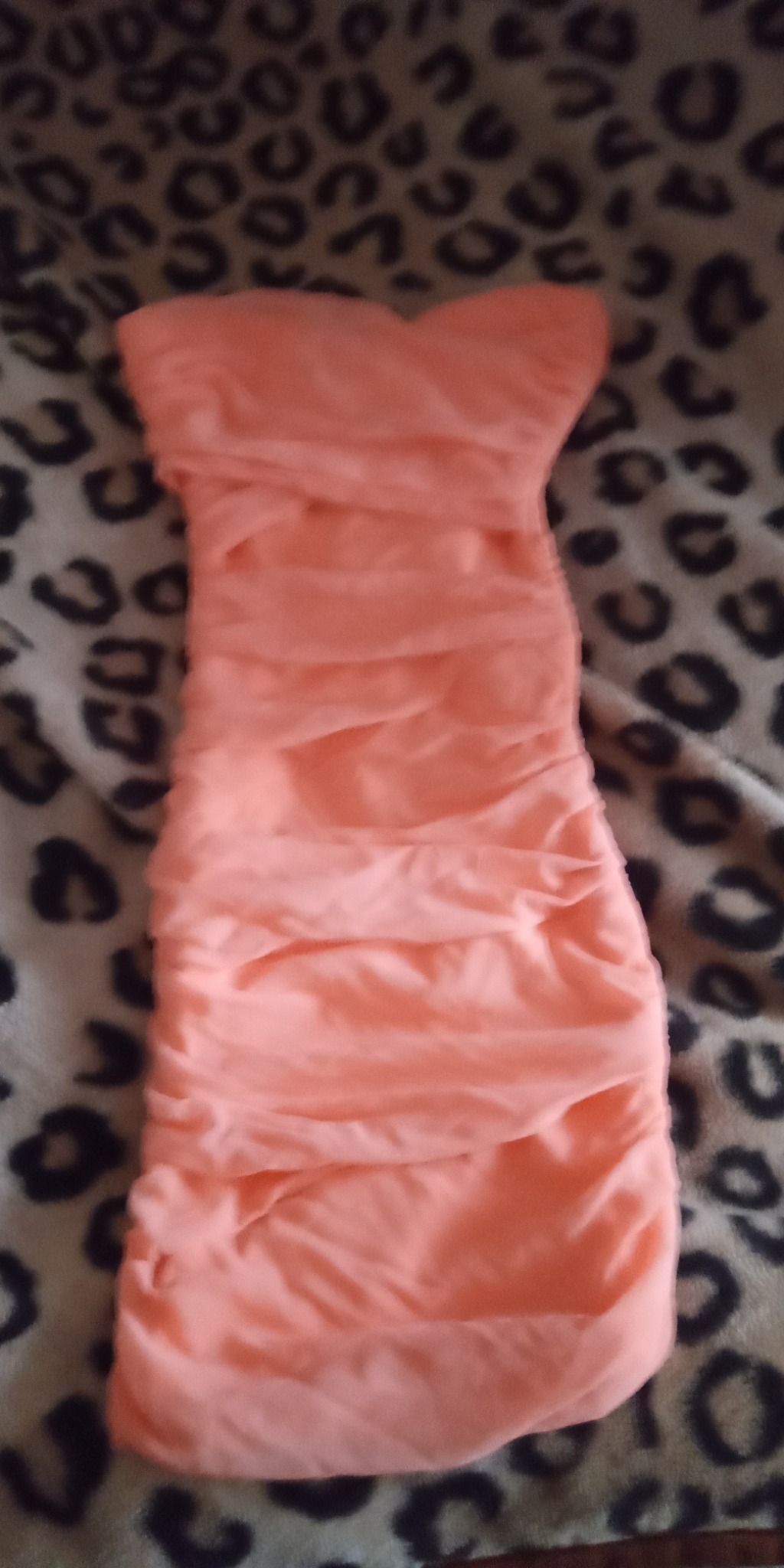 Pomarańczowa, drapowana sukienka bez ramiączek leżąca na kocu w panterkę.